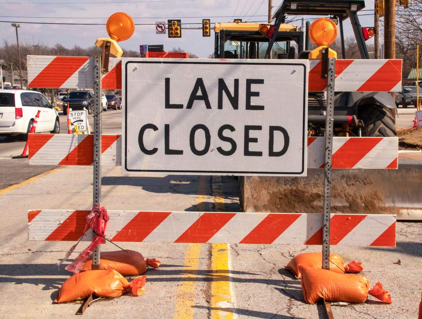 Lane Closed sign at messy construction urban intersection with sand bags traffic cones heavy equipment working and cars stopped at stoplight. Concept: 215 Beltway construction