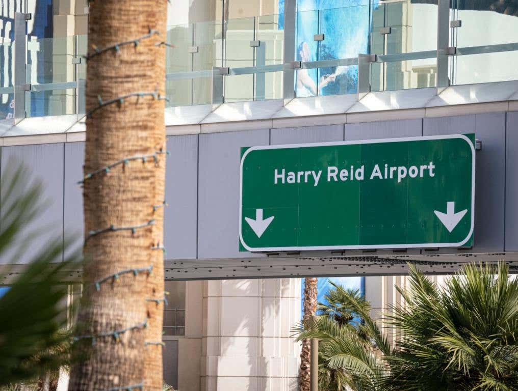 Green traffic sign for Harry Reid Las Vegas airport hangs on a bridge with white arrows pointing down.