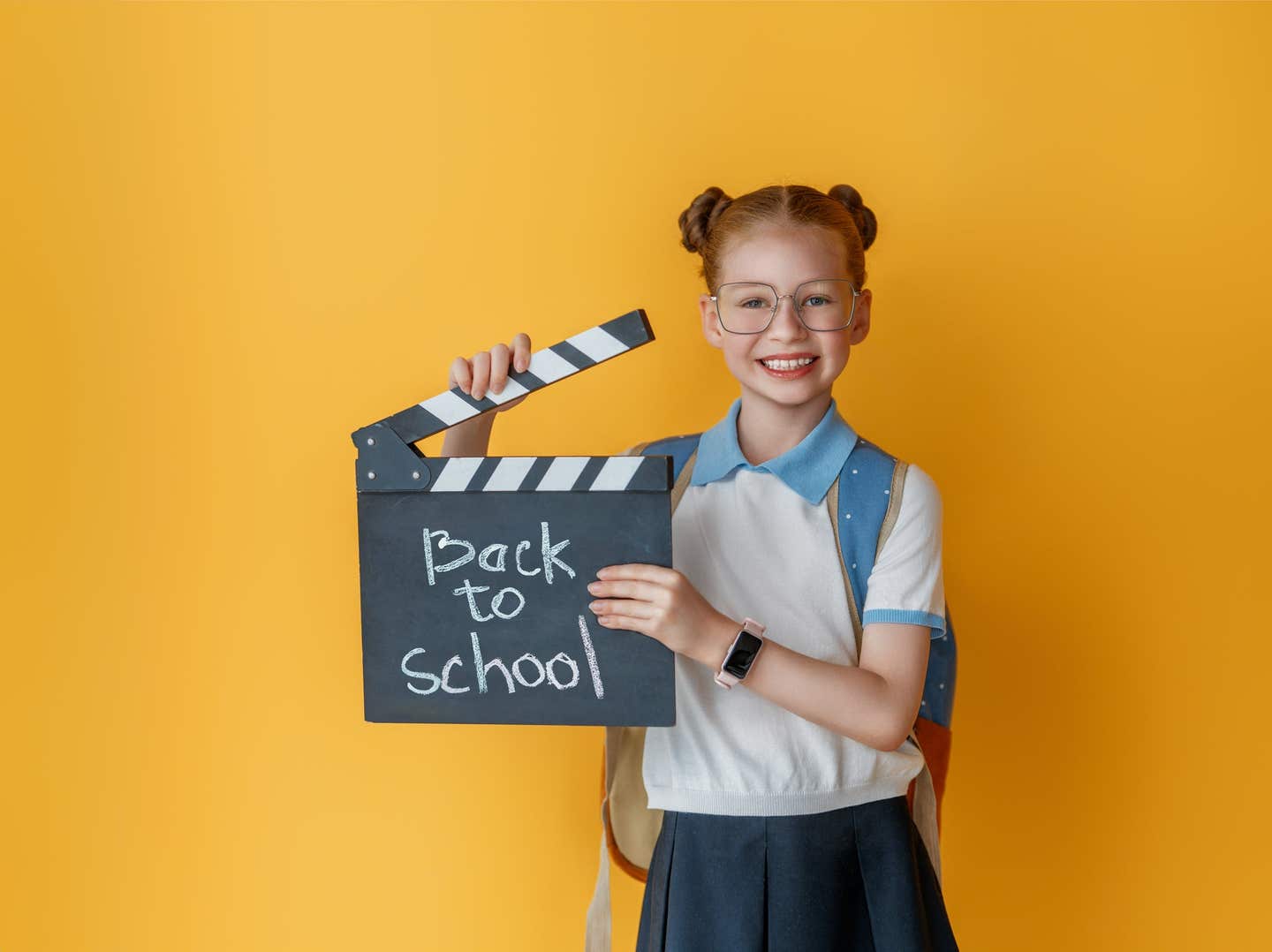 Cute happy teenager standing on bright yellow background. Child with backpack, girl is ready to back to school.